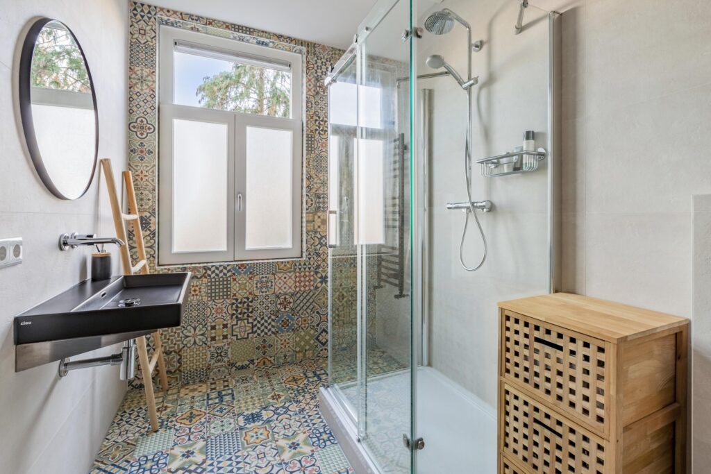 Modern bathroom with colorful tiled walls and glass shower.