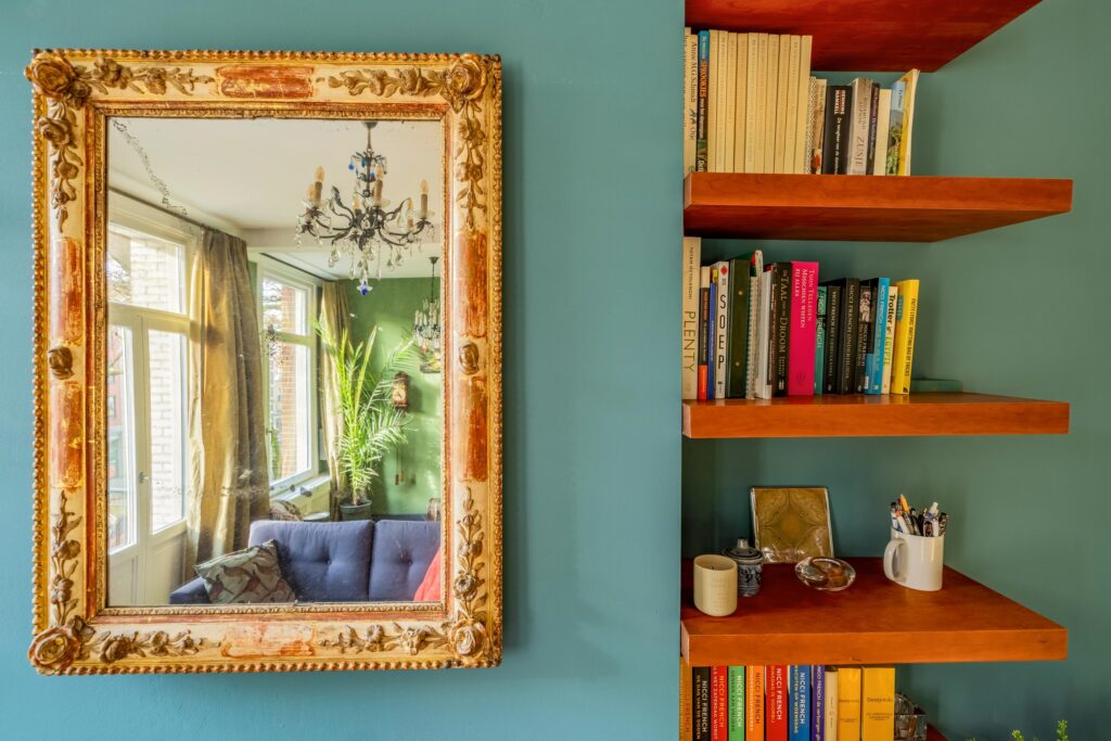 Ornate mirror reflects elegant room, beside bookshelf.