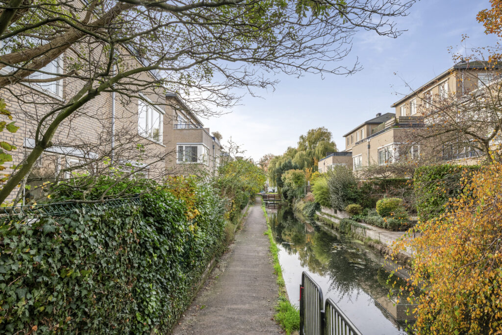 Pathway alongside canal with autumn foliage and houses.