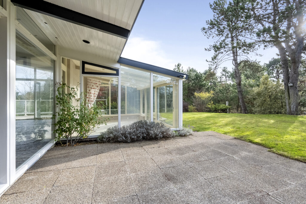 Modern glass house with garden and patio view.