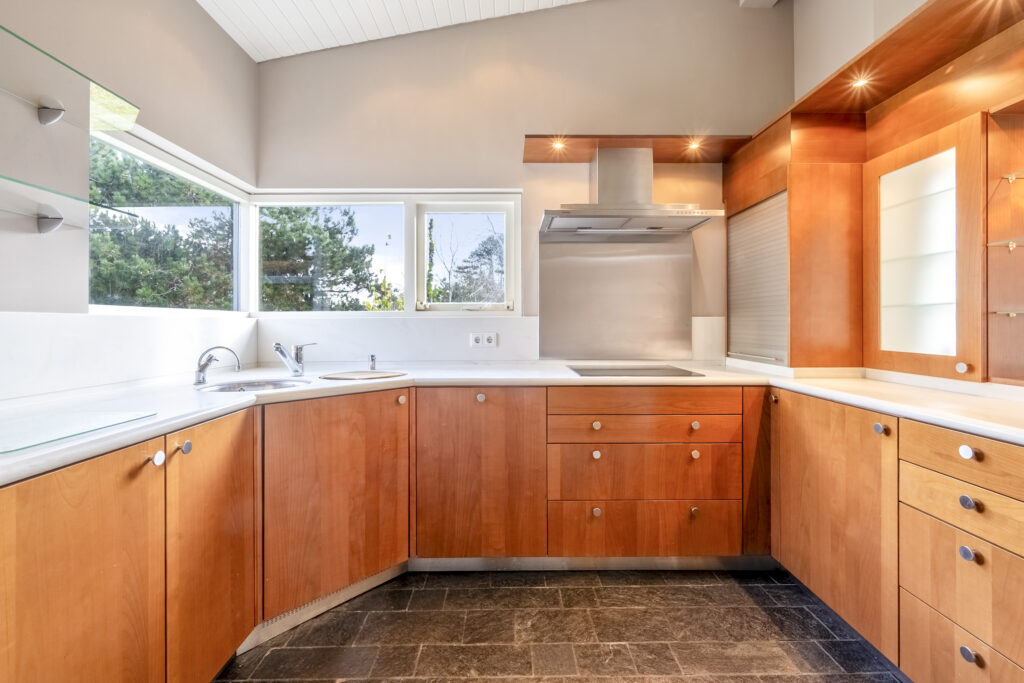 Modern kitchen with wooden cabinets and large windows.