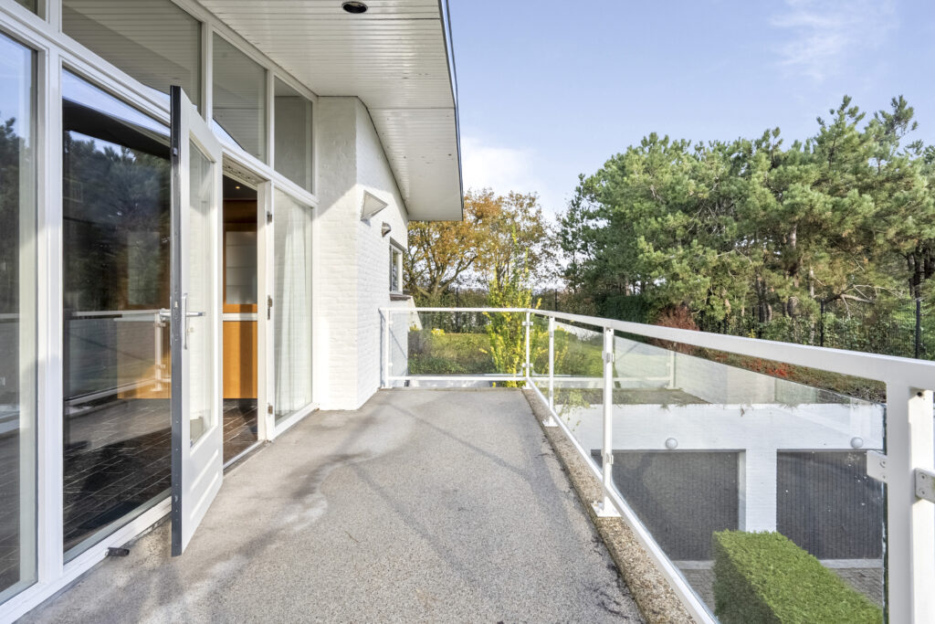 Spacious balcony with glass railing and forest view.