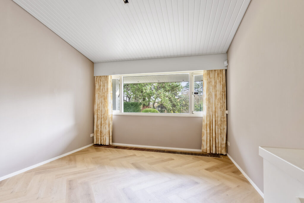 Empty room with large window and beige curtains.