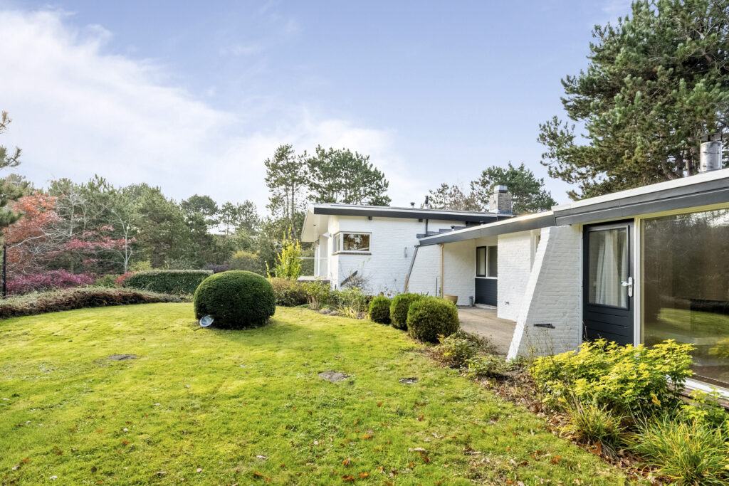 Modern white house with lush garden and trees.