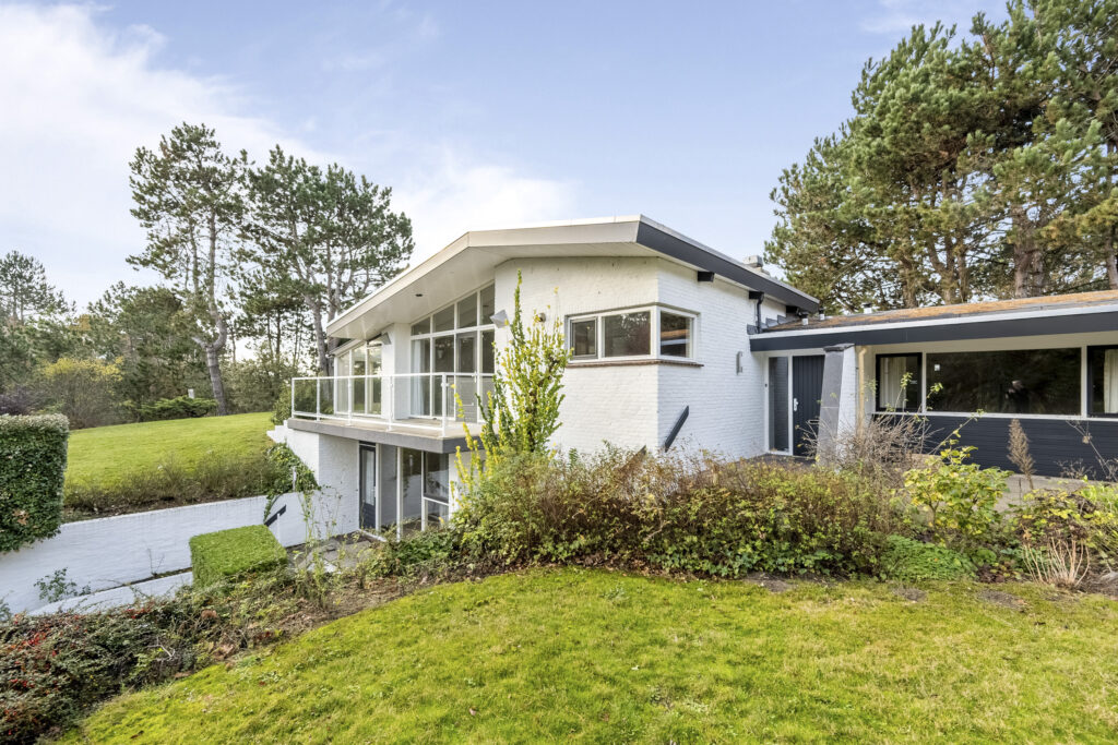 Modern white house with greenery and blue sky.