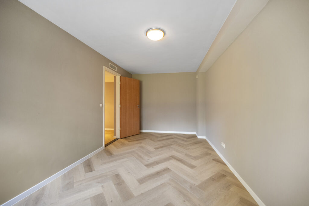 Empty room with herringbone wood floor and open door.