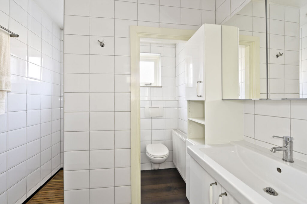 Modern white tiled bathroom with sink and toilet.