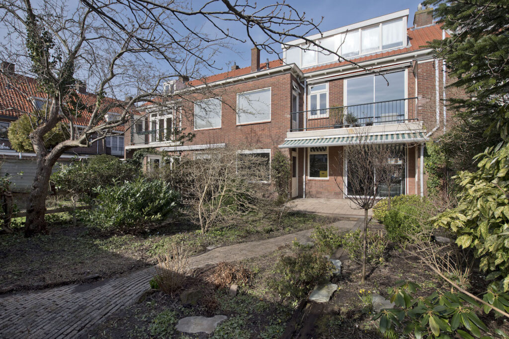 Residential house with garden and bare trees, sunny day.