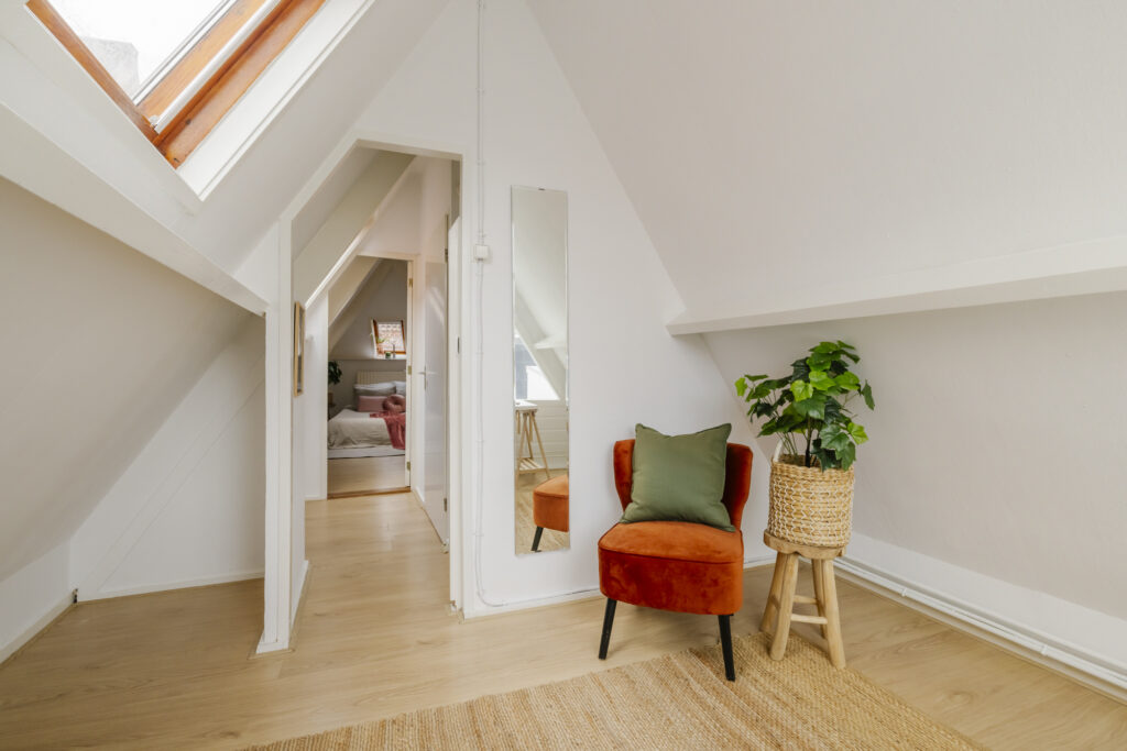 Cozy attic bedroom with chair and plant.