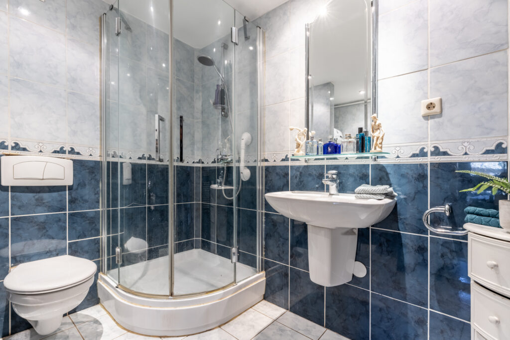 Modern bathroom with glass shower and blue tiles.