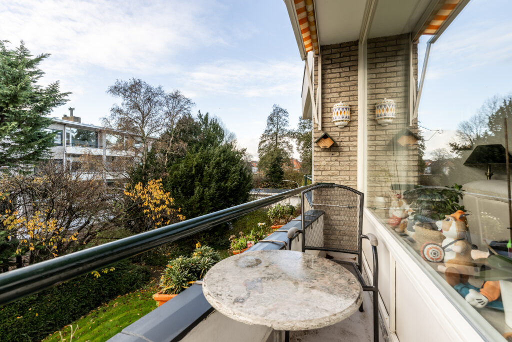 Apartment balcony overlooking garden with trees and plants.