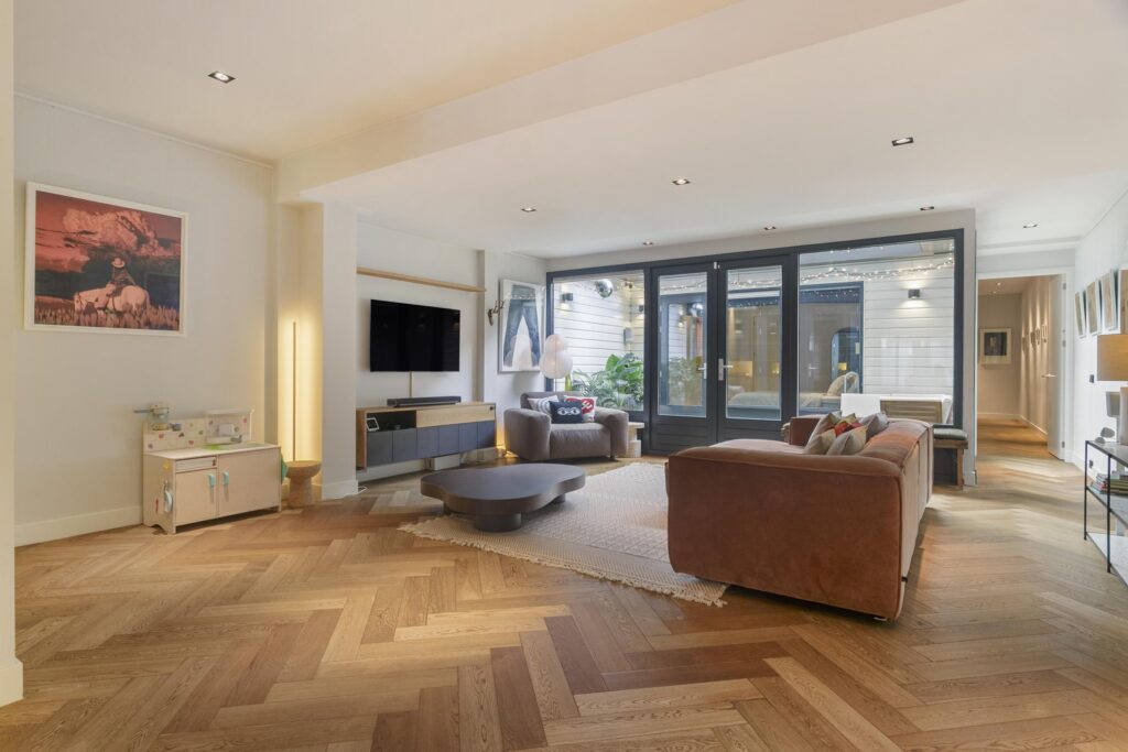Modern living room with hardwood floors and large windows.