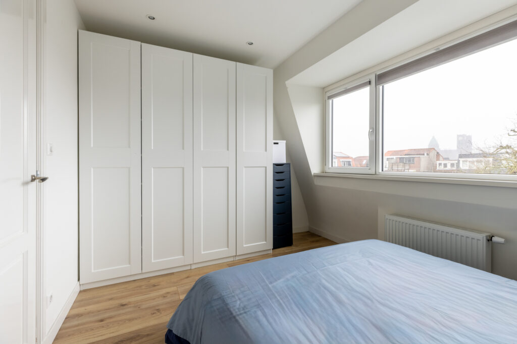 Bright bedroom with wardrobe and large window view.