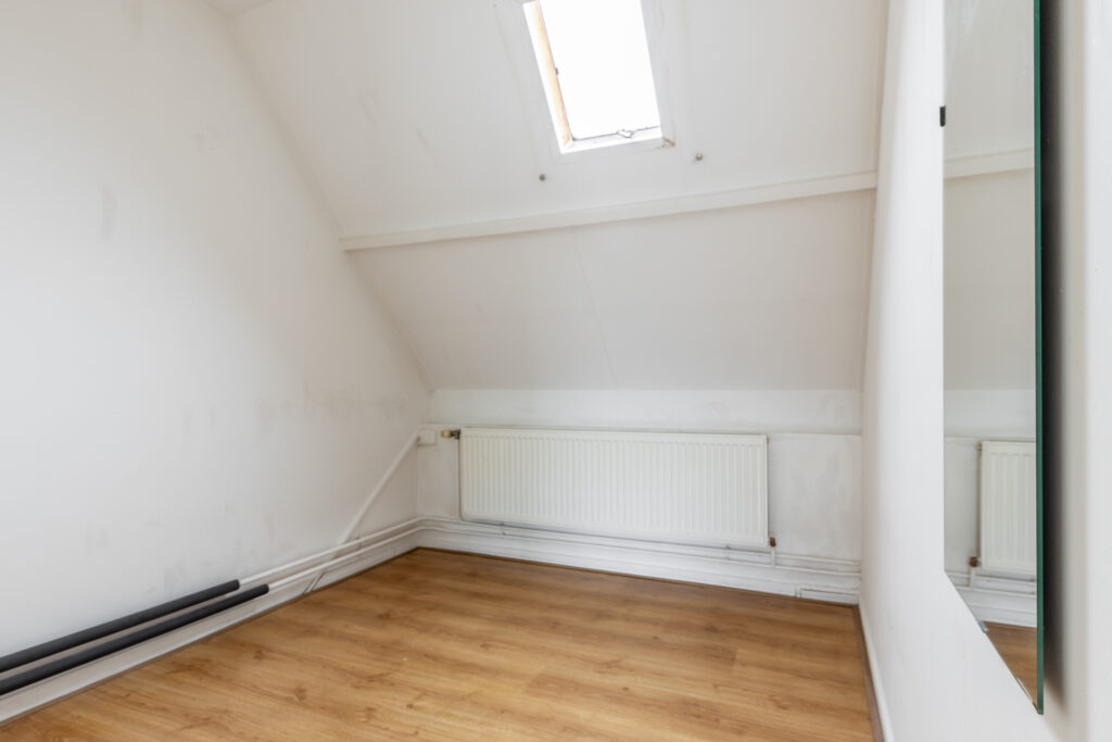 Empty attic room with skylight and radiator.