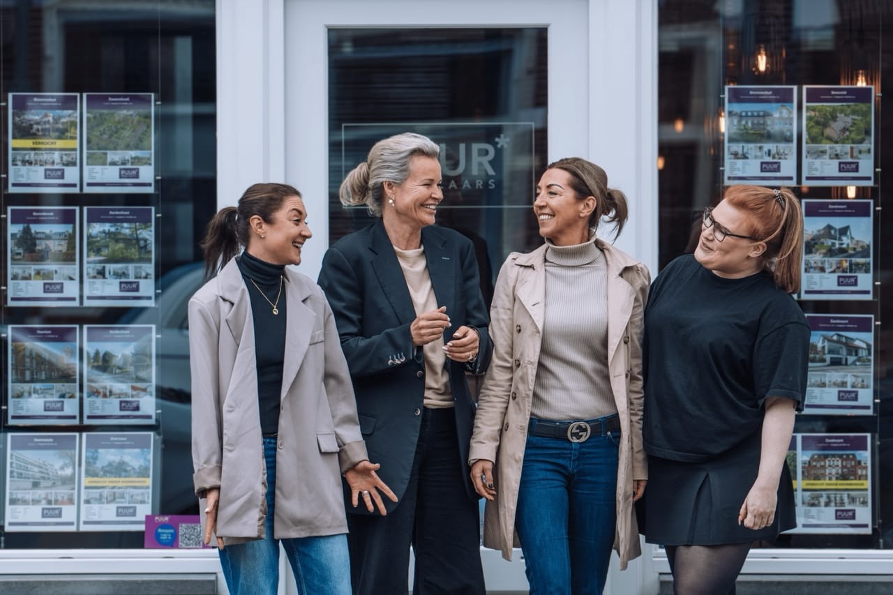 Four women smiling outside a real estate office.